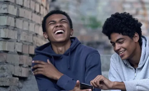 Two friends enjoying a funny moment while checking their phones